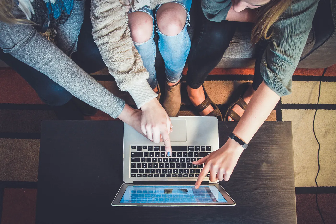 Three people huddled around a laptop pointing at the screen. The picture has been taken from bird-eye view. 